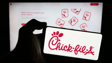 Stuttgart, Almanya - 04-08-2024: ABD 'li fast food restoran şirketi Chick-fil-A Inc.' in logosuyla cep telefonu sahibi kişi iş sayfasının önünde. Telefon ekranına odaklan.