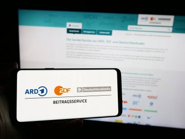 Stuttgart, Almanya - 04-10-2024: İnternet sitesi önünde ARD ZDF Deutschlandradio Beitragsservice logosuna sahip akıllı telefon sahibi kişi. Telefon ekranına odaklan.