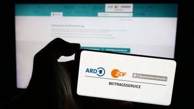 Stuttgart, Almanya - 04-10-2024: İnternet sayfası önünde ARD ZDF Deutschlandradio Beitragsservice logosuna sahip cep telefonu sahibi kişi. Telefon ekranına odaklan.