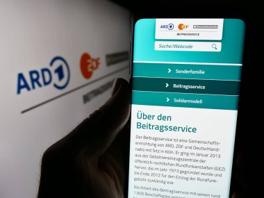 Stuttgart, Almanya - 04-10-2024: Logo önünde ARD ZDF Deutschlandradio Beitragsservice web sitesi ile cep telefonu tutan kişi. Telefon ekranının merkezine odaklan.