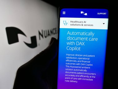Stuttgart, Almanya - 04-10-2024: ABD 'li yazılım şirketi Nuance Communications Inc.' in web sayfası ile logo önünde cep telefonu tutan kişi. Telefon ekranının merkezine odaklan.