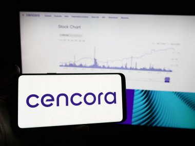 Stuttgart, Almanya - 04-12-2024: Amerikan ilaç toptan şirketi Cencora Inc. 'in logosunu taşıyan cep telefonu sahibi kişi iş sayfasının önünde. Telefon ekranına odaklan.