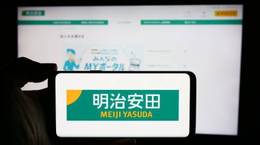 Stuttgart, Almanya - 04-12-2024: Japon iş dünyası Meiji Yasuda Hayat Sigortası Şirketi 'nin logosunun bulunduğu cep telefonu sahibi kişi iş sayfası önünde. Telefon ekranına odaklan.