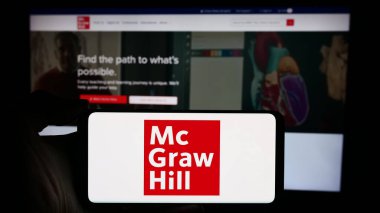 Stuttgart, Almanya - 04-12-2024: ABD 'li yayıncılık şirketi McGraw Hill LLLC' nin logosuyla cep telefonu sahibi kişi iş sayfası önünde. Telefon ekranına odaklan.
