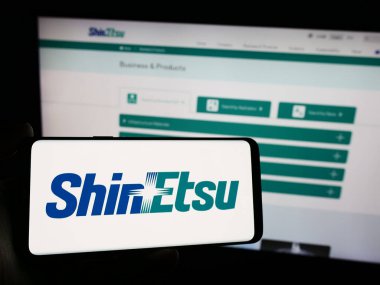 Stuttgart, Almanya - 04-13-2024: Japon kimya şirketi Shin-Etsu Chemical Co. Ltd. web sitesinin önünde elinde akıllı telefon bulunan kişi. Telefon ekranına odaklan.