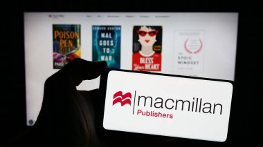 Stuttgart, Almanya - 04-13-2024: İngiliz yayıncılık şirketi Macmillan Publishers 'ın logosuyla cep telefonu sahibi kişi iş sayfası önünde. Telefon ekranına odaklan.