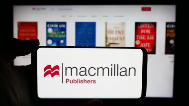 Stuttgart, Almanya - 04-13-2024: İngiliz yayıncılık şirketi Macmillan Publishers 'ın logosuyla cep telefonu tutan kişi iş sayfası önünde. Telefon ekranına odaklan.