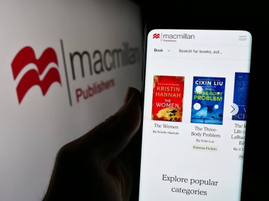 Stuttgart, Almanya - 04-13-2024: İngiliz yayıncılık şirketi Macmillan Publishers 'ın web sayfası ile logo önünde cep telefonu tutan kişi. Telefon ekranının merkezine odaklan.
