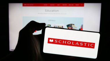 Stuttgart, Almanya - 04-13-2024: Amerikan yayıncılık şirketi Scholastic Corporation 'ın logosuna sahip cep telefonu sahibi kişi iş sayfasının önünde. Telefon ekranına odaklan.