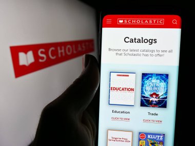 Stuttgart, Almanya - 04-13-2024: ABD 'li yayıncılık şirketi Scholastic Corporation' ın web sayfası ile logo önünde cep telefonu tutan kişi. Telefon ekranının merkezine odaklan.