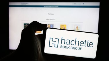 Stuttgart, Almanya - 04-13-2024: İnternet sayfası önünde Amerikan yayıncılık şirketi Hachette Book Inc. (HBG) logosuna sahip cep telefonu sahibi kişi. Telefon ekranına odaklan.