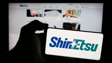 Stuttgart, Almanya - 04-13-2024: Japon kimya şirketi Shin-Etsu Chemical Co. Ltd. nin logosuyla cep telefonu tutan kişi web sayfasının önünde. Telefon ekranına odaklan.