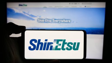 Stuttgart, Germany - 04-13-2024: Person holding mobile phone with logo of Japanese chemicals company Shin-Etsu Chemical Co. Ltd. in front of web page. Focus on phone display. clipart