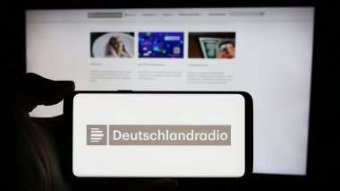 Stuttgart, Almanya - 04-13-2024: İnternet sayfası önünde Alman devlet radyo kanalı Deutschlandradio 'nun logosuna sahip kişi. Telefon ekranına odaklan.