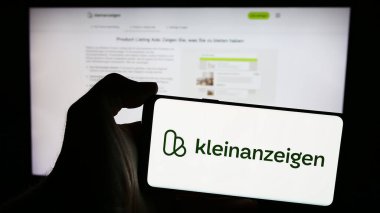 Stuttgart, Almanya - 04-13-2024: Üzerinde Almanca sınıflandırılmış platform şirketi Kleinanzeigen.de GmbH 'nin logosu bulunan cep telefonu sahibi kişi web sayfası önünde. Telefon ekranına odaklan.