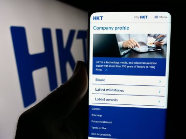 Stuttgart, Germany - 04-13-2024: Person holding smartphone with webpage of telecommunications company HKT Limited (Hong Kong Telecom) with logo. Focus on center of phone display. clipart