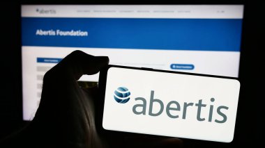 Stuttgart, Almanya - 04-13-2024: İnternet sitesi önünde üzerinde İspanyol gişe şirketi Abertis Infraestructuras SA 'nın logosu bulunan cep telefonu sahibi kişi. Telefon ekranına odaklan.