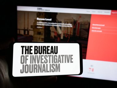 Stuttgart, Almanya - 04-13-2024: İnternet sayfası önündeki The Bureau of Investigative Journalism (TBIJ) örgütünün logosuyla cep telefonu tutan kişi. Telefon ekranına odaklan.