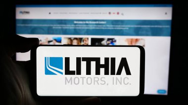 Stuttgart, Almanya - 04-13-2024: ABD otomotiv bayiliği şirketi Lithia Motors Inc. 'in logosunun bulunduğu cep telefonu sahibi kişi iş sayfasının önünde. Telefon ekranına odaklan.