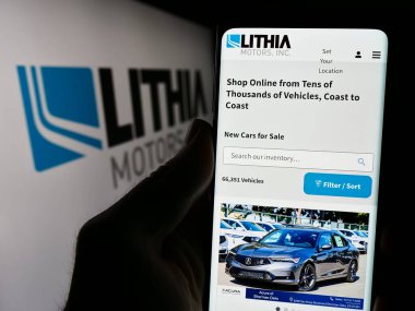 Stuttgart, Almanya - 04-13-2024: ABD otomotiv bayiliği şirketi Lithia Motors Inc. 'in web sayfası ile logo önünde cep telefonu tutan kişi. Telefon ekranının merkezine odaklan.