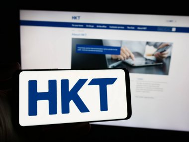 Stuttgart, Almanya - 04-13-2024: İnternet sitesi önünde üzerinde telekomünikasyon şirketi HKT Limited (Hong Kong Telekom) logosu bulunan kişi. Telefon ekranına odaklan.