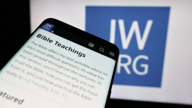 Stuttgart, Germany - 04-15-2024: Smartphone with website of religious organisation Jehovah's Witnesses in front of logo. Focus on top-left of phone display. clipart