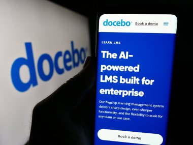 Stuttgart, Almanya - 04-17-2024: Kanadalı öğrenim yazılım şirketi Docebo Inc. 'nin web sitesi ile logo önünde cep telefonu tutan kişi. Telefon ekranının merkezine odaklan.