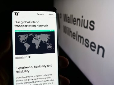 Stuttgart, Almanya - 04-17-2024: Nakliye şirketi Wallenius Wilhelmsen ASA 'nın internet sayfası ile logo önünde cep telefonu tutan kişi. Telefon ekranının merkezine odaklan.
