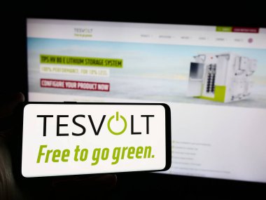 Stuttgart, Almanya - 04-17-2024: Alman enerji depolama şirketi TESVOLT AG 'nin logosuna sahip cep telefonu sahibi kişi iş sayfasının önünde. Telefon ekranına odaklan.