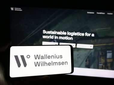 Stuttgart, Almanya - 04-17-2024: Deniz taşımacılığı şirketi Wallenius Wilhelmsen ASA 'nın logosuna sahip akıllı telefon sahibi kişi web sitesinin önünde. Telefon ekranına odaklan.