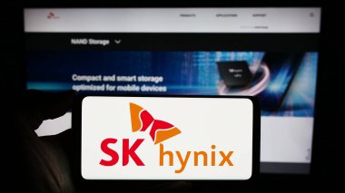 Stuttgart, Almanya - 11-16-2023: Güney Koreli yarı iletken şirket SK hynix Inc. 'in logosuna sahip cep telefonu sahibi kişi iş sayfasının önünde. Telefon ekranına odaklan.