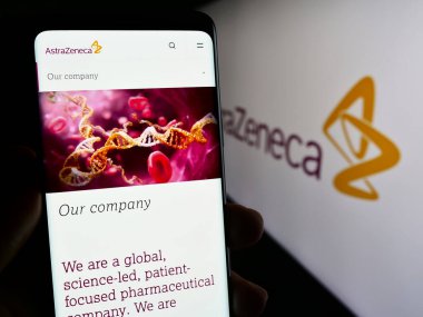 Stuttgart, Almanya - 11-16-2023: Eczacılık şirketi AstraZeneca plc 'nin internet sayfası ile birlikte iş logosu önünde cep telefonu tutan kişi. Telefon ekranının merkezine odaklan.