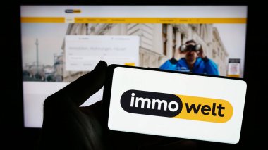 Stuttgart, Almanya - 11-16-2023: Alman emlak platformu şirketi Immowelt GmbH 'in logosuna sahip akıllı telefon sahibi kişi web sitesinin önünde. Telefon ekranına odaklan.