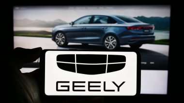 Stuttgart, Almanya - 11-16-2023: Çinli otomobil üreticisi Zhejiang Geely Holding Group 'un logosuyla cep telefonu tutan kişi iş sayfasının önünde. Telefon ekranına odaklan.