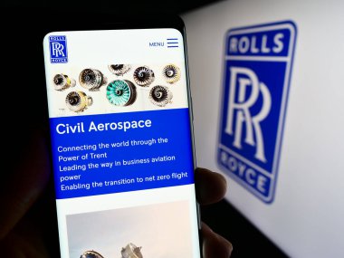 Stuttgart, Almanya - 11-16-2023: İngiliz havacılık şirketi Rolls-Royce Holding plc 'un web sayfası ile logo önünde cep telefonu tutan kişi. Telefon ekranının merkezine odaklan.