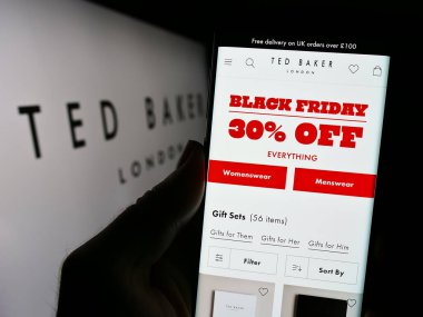 Stuttgart, Almanya - 11-16-2023: İngiliz giyim perakende şirketi Ted Baker plc 'in web sayfası ile logo önünde cep telefonu tutan kişi. Telefon ekranının merkezine odaklan.