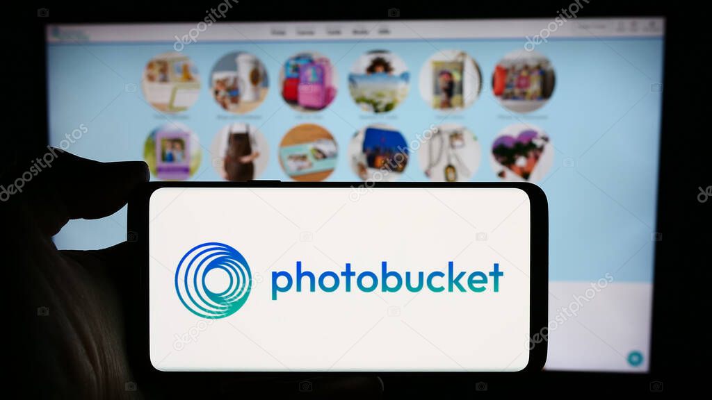 Stuttgart, Germany - 04-15-2024: Person holding cellphone with logo of US image hosting company Photobucket.com Inc. in front of business webpage. Focus on phone display.