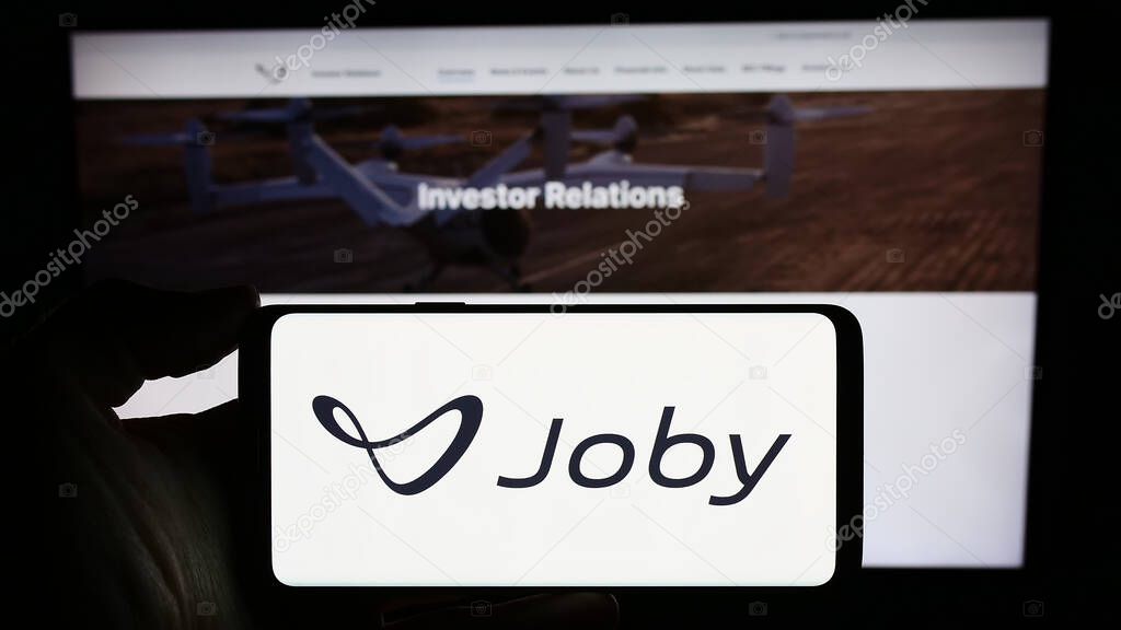 Stuttgart, Germany - 11-16-2023: Person holding smartphone with logo of US eVTOL aircraft company Joby Aviation in front of website. Focus on phone display.