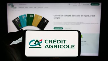 Stuttgart, Almanya - 11-16-2023: Fransız finans hizmetleri şirketi Credit Agricole SA 'nın logosuna sahip cep telefonu sahibi kişi iş sayfasının önünde. Telefon ekranına odaklan.
