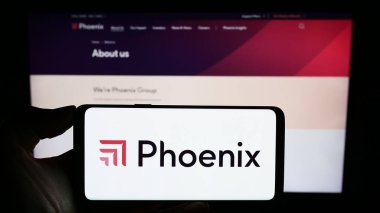Stuttgart, Almanya - 11-17-2023: İngiliz sigorta şirketi Phoenix Group Holding 'in logosunun bulunduğu cep telefonu sahibi kişi iş sayfasının önünde. Telefon ekranına odaklan.