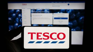 Stuttgart, Almanya - 11-17-2023: İngiliz market perakende şirketi Tesco plc 'nin logosuna sahip akıllı telefon sahibi kişi web sitesinin önünde. Telefon ekranına odaklan.