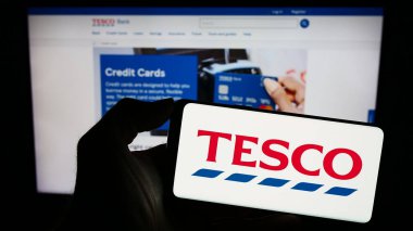 Stuttgart, Almanya - 11-17-2023: İngiliz market perakende şirketi Tesco plc 'nin logosunun bulunduğu cep telefonu sahibi kişi iş sayfasının önünde. Telefon ekranına odaklan.