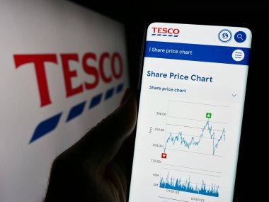 Stuttgart, Almanya - 11-17-2023: İngiliz market perakende şirketi Tesco plc 'in internet sayfası olan cep telefonu sahibi şirket logosu önünde. Telefon ekranının merkezine odaklan.