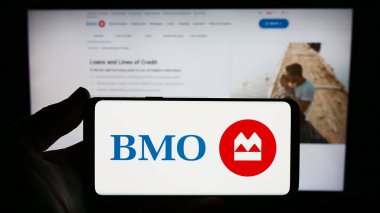 Stuttgart, Almanya - 11-17-2023: Kanadalı finans hizmetleri şirketi Bank of Montreal 'in (BMO) logosuna sahip akıllı telefon sahibi kişi web sitesinin önünde. Telefon ekranına odaklan.