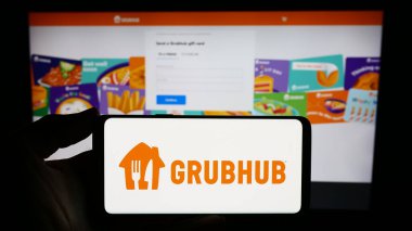 Stuttgart, Germany - 11-22-2023: Person holding smartphone with logo of US food ordering and delivery company Grubhub Inc. in front of website. Focus on phone display. clipart