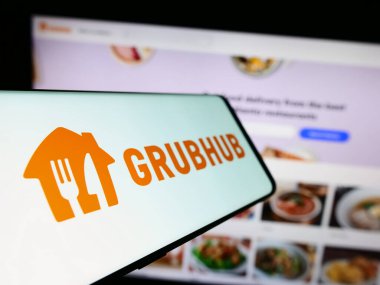 Stuttgart, Germany - 11-22-2023: Mobile phone with logo of American food ordering and delivery company Grubhub Inc. in front of website. Focus on center-left of phone display. clipart