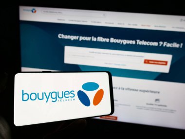 Stuttgart, Almanya - 11-22-2023: İnternet sayfası önünde Fransız telekomünikasyon şirketi Bouygues Telecom S.A. 'nın logosuna sahip cep telefonu sahibi kişi. Telefon ekranına odaklan.
