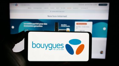 Stuttgart, Almanya - 11-22-2023: Fransız telekomünikasyon şirketi Bouygues Telecom SA 'nın logosuna sahip cep telefonu sahibi kişi iş sayfasının önünde. Telefon ekranına odaklan.