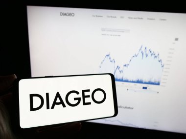 Stuttgart, Almanya - 11-22-2023: İngiliz alkolik içecek şirketi Diageo plc 'nin logosunu taşıyan cep telefonu sahibi kişi iş sayfasının önünde. Telefon ekranına odaklan.