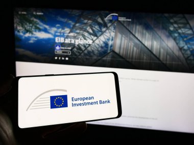 Stuttgart, Almanya - 11-22-2023: İnternet sayfası önünde AB finans kurumu Avrupa Yatırım Bankası 'nın (EIB) logosuna sahip cep telefonu sahibi kişi. Telefon ekranına odaklan.